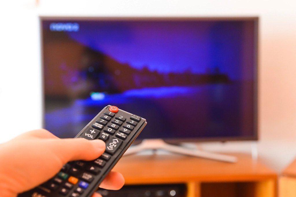 A hand pointing a remote at a glowing TV at home