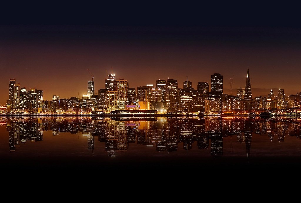 A city skyline at night reflected in the water